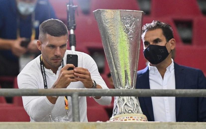 German football player Lucas podolski (L) photographs the trophy prior to the UEFA Europa League semi-final football match Sevilla v Manchester United on August 16, 2020 in Cologne, western Germany.  Martin Meissner / POOL / AFP