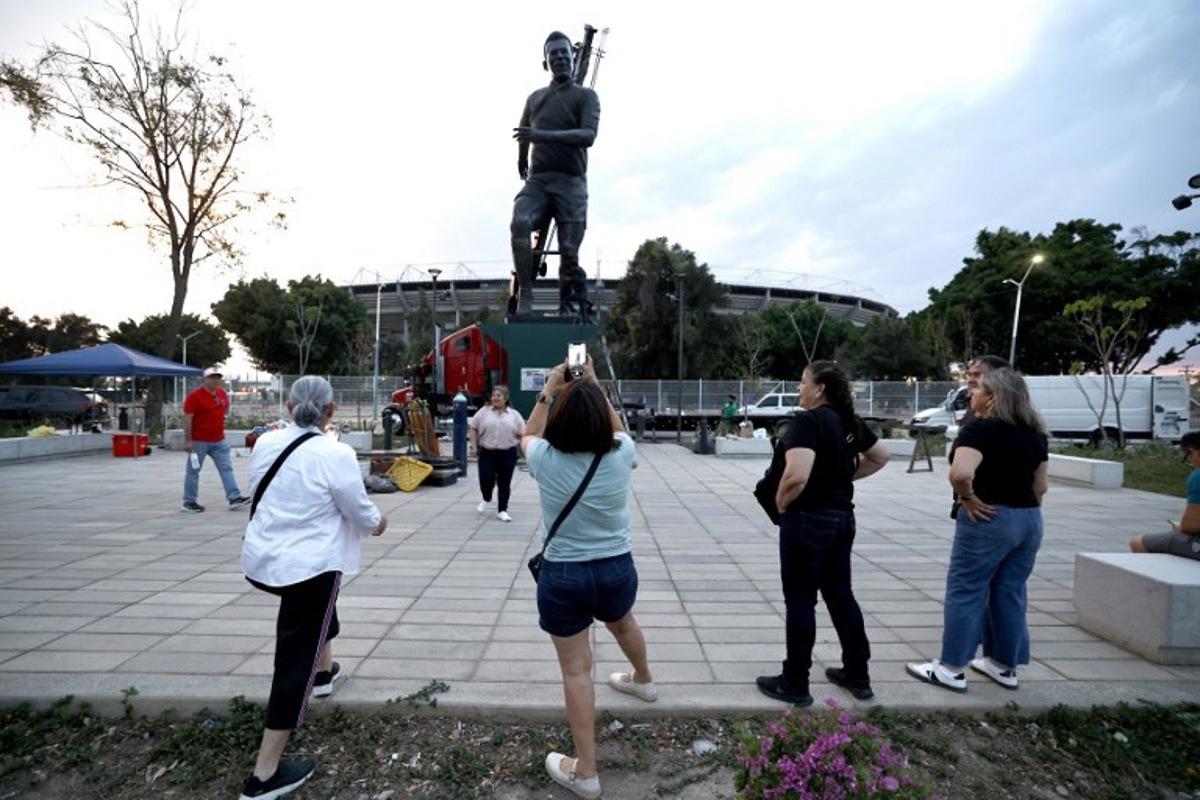 People take pictures as workers place a sculpture of late Brazilian football legend Pele, by artist Alejandro Velazco, called "La Canarinha" on the esplanade of the Jalisco Stadium in Guadalajara, Jalisco, Mexico, on May 17, 2026. The three-ton, 9-meter-high statue made of silver nitrate bronze was placed at Jalisco stadium as part of the events of the 2026 FIFA World Cup to be held in Mexico. ULISES RUIZ / AFP
