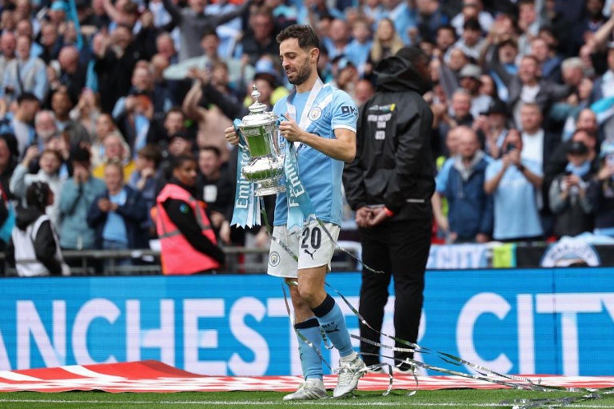 Manchester City's Portuguese midfielder #20 Bernardo Silva holds the trophy as City players celebrate on the pitch after the English FA Cup final football match between Chelsea and Manchester City at Wembley stadium in London, on May 16, 2026. Manchester City won the game 1-0. The third FA Cup success of Guardiola's reign ended City's run of two successive defeats in the final. Adrian Dennis / AFP