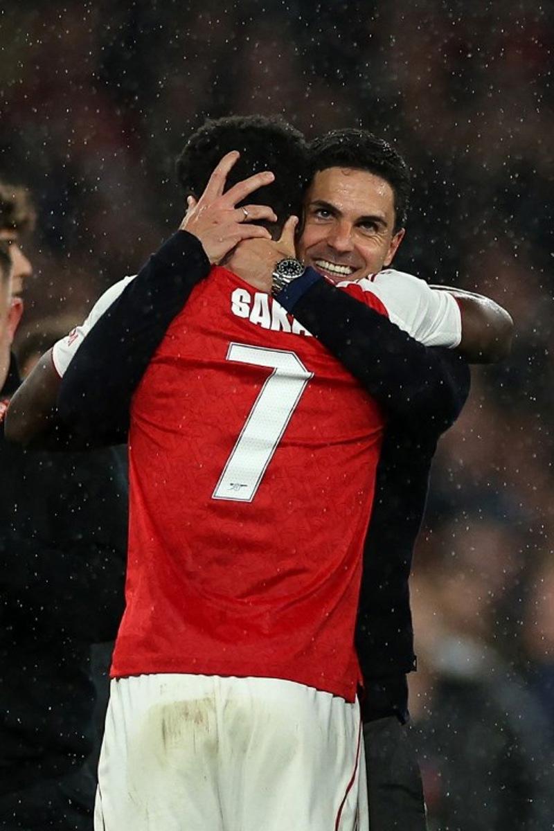 Arsenal's Spanish manager Mikel Arteta hugs Arsenal's English midfielder #07 Bukayo Saka after winning the UEFA Champions League second-leg semi-final football match between Arsenal and Atletico Madrid at the Emirates Stadium in north London on May 5, 2026.  Adrian Dennis / AFP
