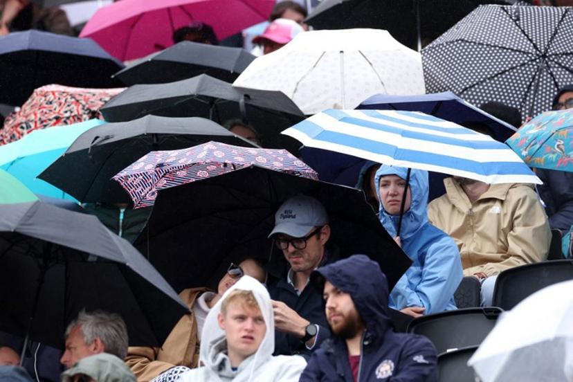 People shelter under umbrella's as a rain delay suspends the round of 32, singles match at the HSBC WTA tennis Championships at Queen's Club in west London on June 8, 2026.  Adrian Dennis / AFP