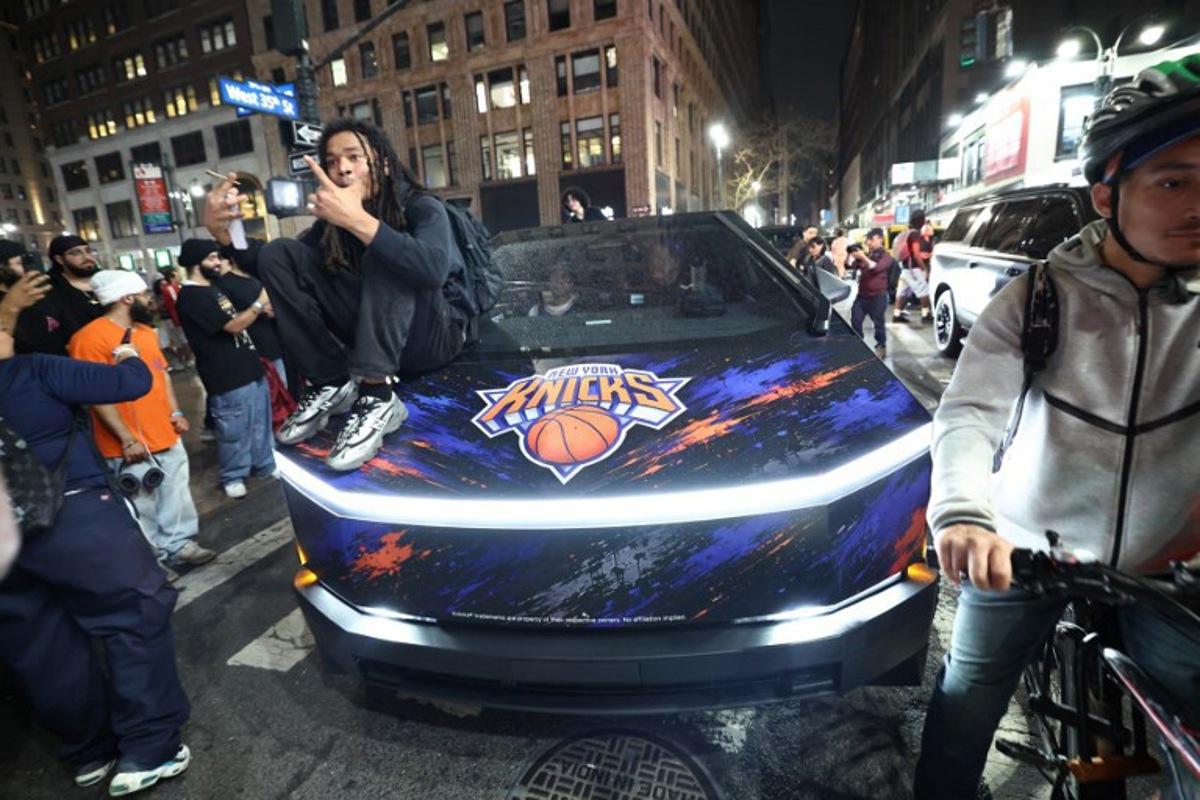A Knicks fan sits on the hood of a car with Knicks stickers in New York, on June 10, 2026 during game four of the NBA Finals between the San Antonio Spurs and the New York Knicks.  CHARLY TRIBALLEAU / AFP