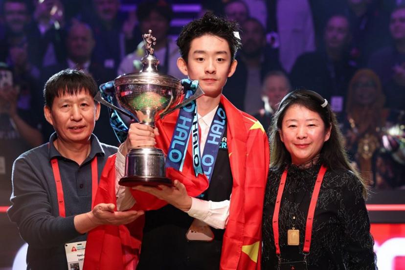 China's Wu Yize (C) holds the championship trophy as he poses with his parents during the awards ceremony after his victory over England's Shaun Murphy in the World Snooker Championship final round at The Crucible in Sheffield, northern England on May 4, 2026.   Darren Staples / AFP