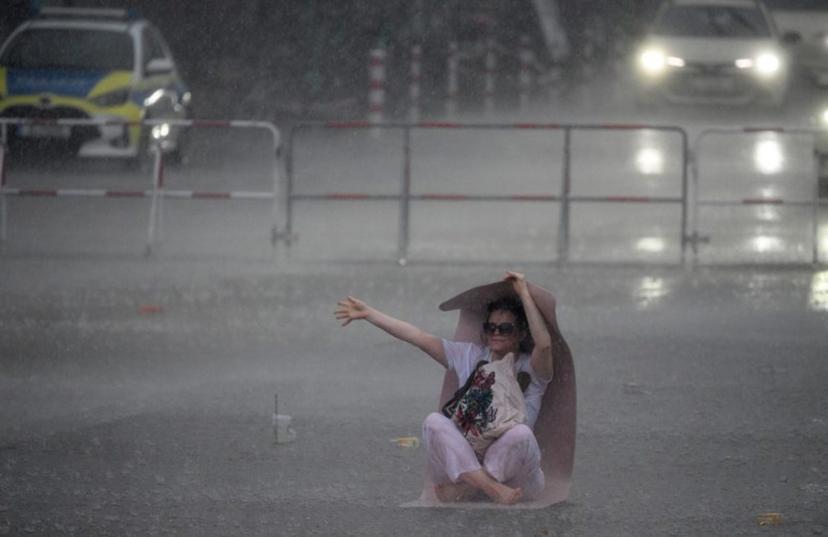 A woman uses a yoga mat to take shelter from the pouring rain as she takes part in the international yoga day, on June 21, 2026 in Berlin, Germany.  RALF HIRSCHBERGER / AFP