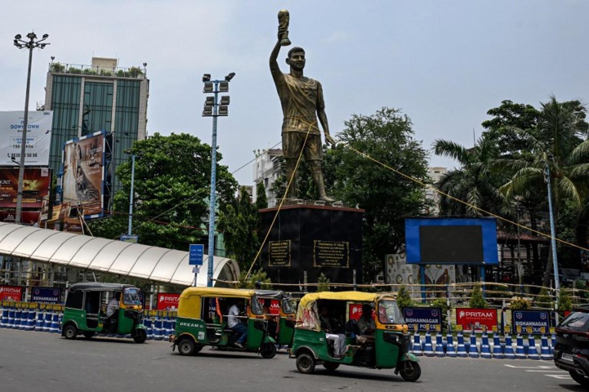 Rickshaws drive past a statue of Argentine football player Lionel Messi that has been tied with rope for stability from rain and thunderstorms, prior to its re-installation in a safer place, in Kolkata on May 27, 2026.  Messi inaugurated the statue virtually during his visit to the city in December 2025. Dibyangshu SARKAR / AFP