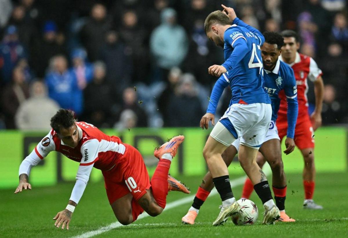 Sporting Braga's Uruguayan midfielder #10 Rodrigo Zalazar (L) falls to the pitch following a challenge from Rangers' Belgian midfielder #43 Nicolas Raskin during the UEFA Europa League league-stage football match between Rangers and CS Braga at the Ibrox Stadium in Glasgow on November 27, 2025. ANDY BUCHANAN / AFP