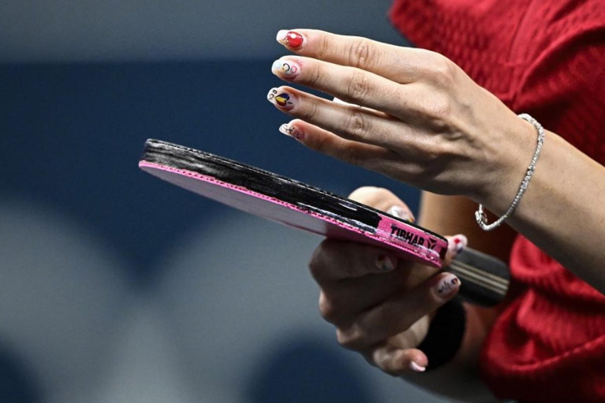 The nails of Romania's Bernadette Szocs depicting a table tennis racket, the Olympic Rings and Romania's national flag are pictured during her mixed table tennis doubles quarter-final with Romania's Ovidiu Ionescu against South Korea's Lim Jonghoon and South Korea's Shin Yubin at the Paris 2024 Olympic Games at the South Paris Arena in Paris on July 27, 2024. WANG Zhao / AFP