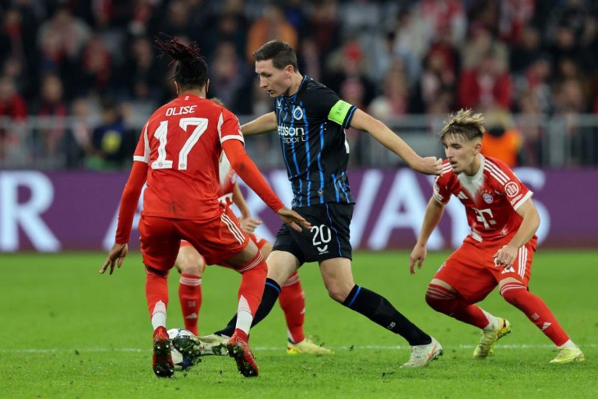 Club Brugge's Belgian midfielder #20 Hans Vanaken (C) vies for the ball with Bayern Munich's French midfielder #17 Michael Olise (L) and Bayern Munich's German midfielder #42 Lennart Karl during the UEFA Champions League football match between FC Bayern Munich and Club Brugge in Munich, southern Germany on October 22, 2025. Alexandra BEIER / AFP