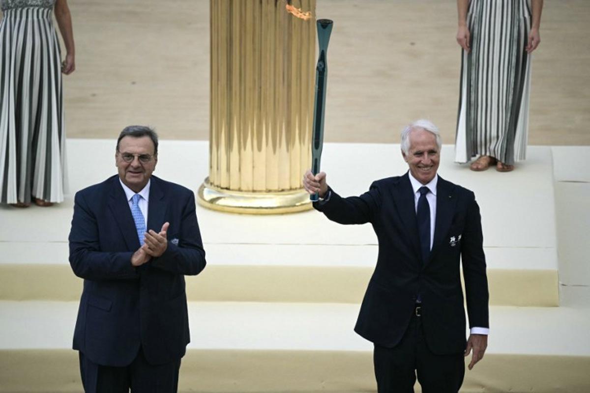 Hellenic Olympic Committee President Isidoros Kouvelos applauds as President of the Italian National Olympic Committee and CEO of the Milan Cortina 2026 Winter Olympic Giovanni Malago (R) hands the torch during the handover Olympic flame ceremony for the Milano-Cortina 2026 Winter Olympic Games and Paralympic Games, at the Panathinean stadium in Athens, on December 4, 2025. Angelos Tzortzinis / AFP